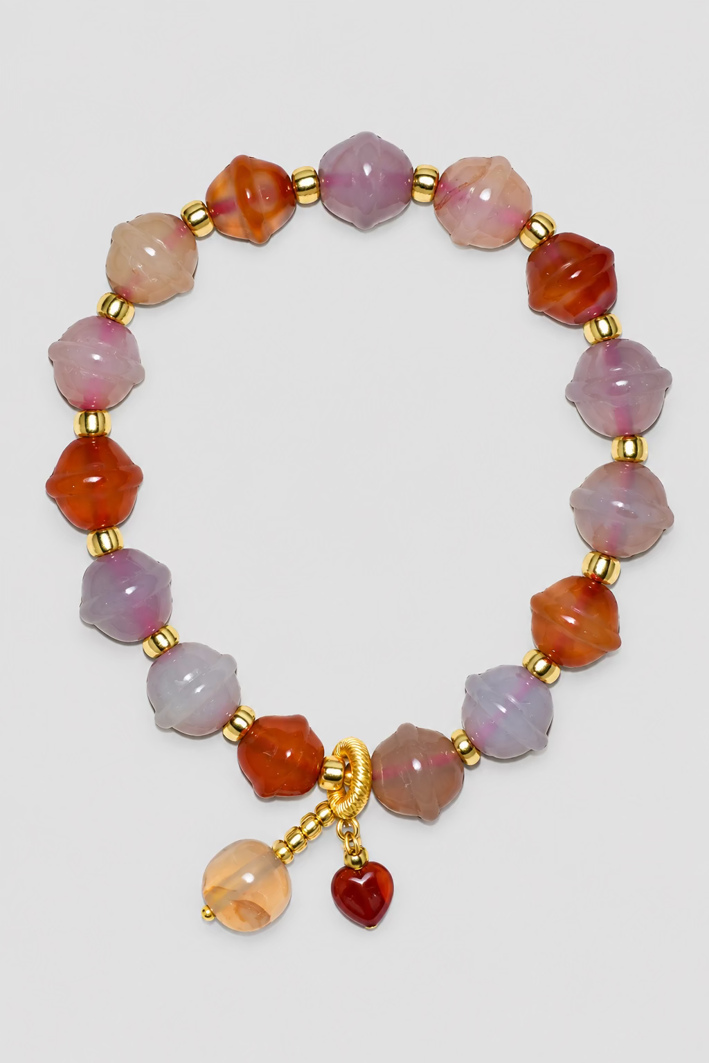 A beaded bracelet featuring faceted translucent beads in shades of pink, orange, and light purple, separated by small gold spacer beads, with a gold clasp and two dangling charms, one beige and one dark red, displayed on a textured light gray background.