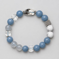 A beaded stretch bracelet featuring light blue and white beads, clear faceted crystal beads, and textured silver-toned spacer accents, displayed on a neutral gray textured background.