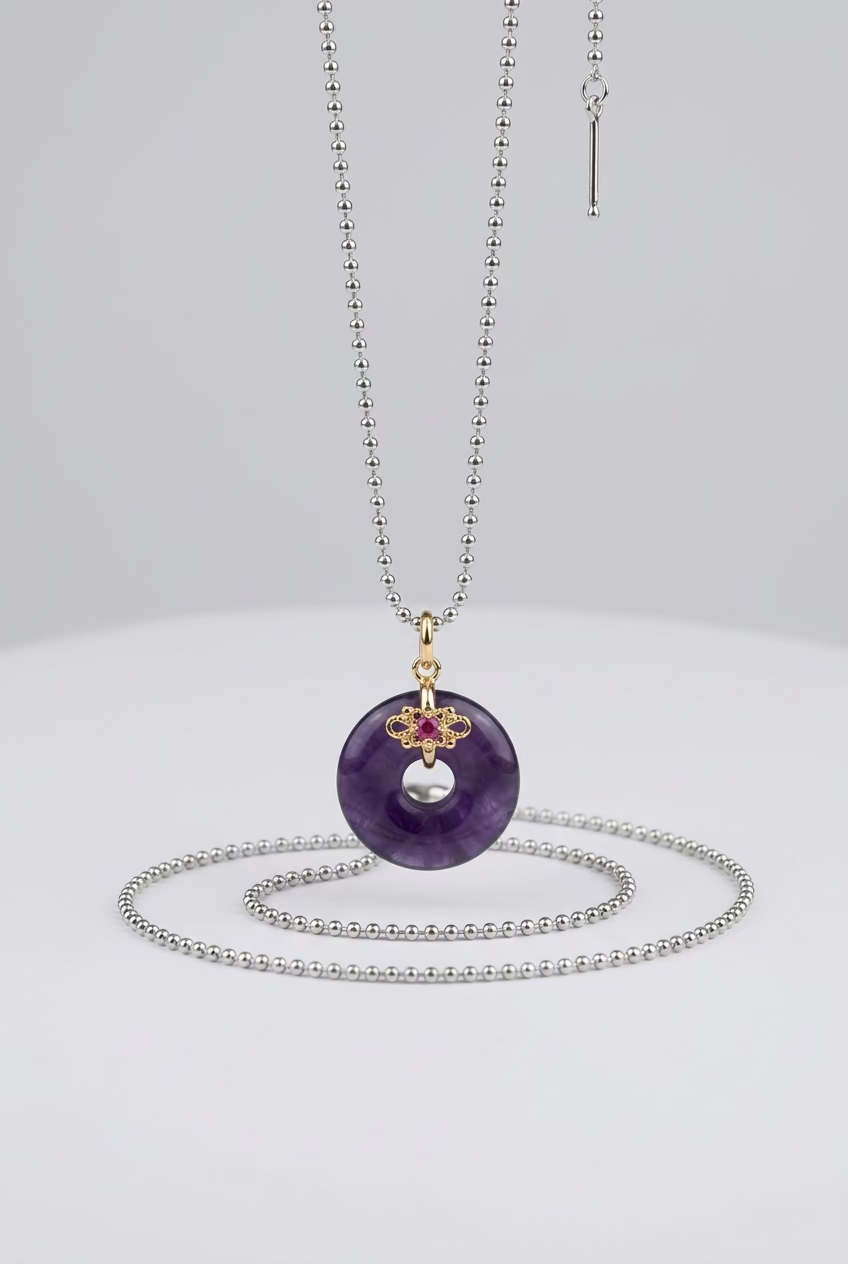 A gold-tone chain necklace with a dark purple donut-shaped pendant, displayed against a textured light gray background.